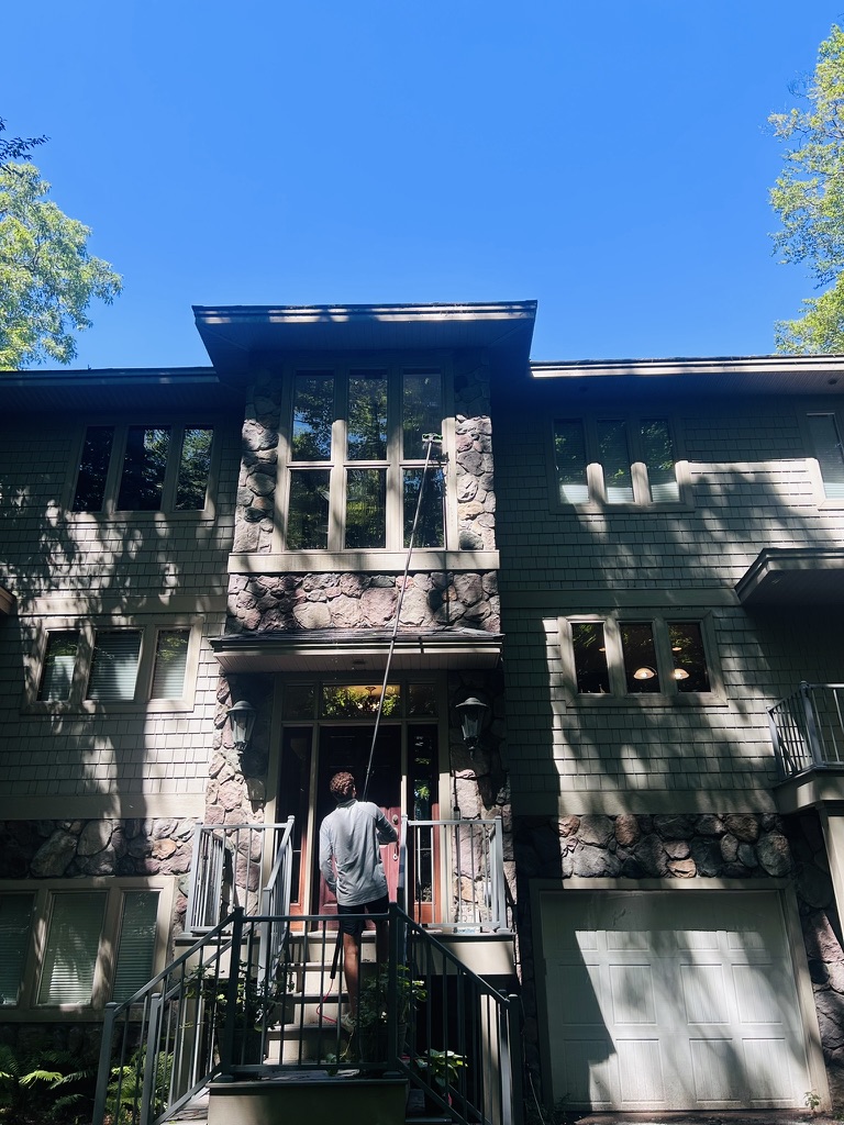 Team member cleaning the front windows of a stone and shingle home